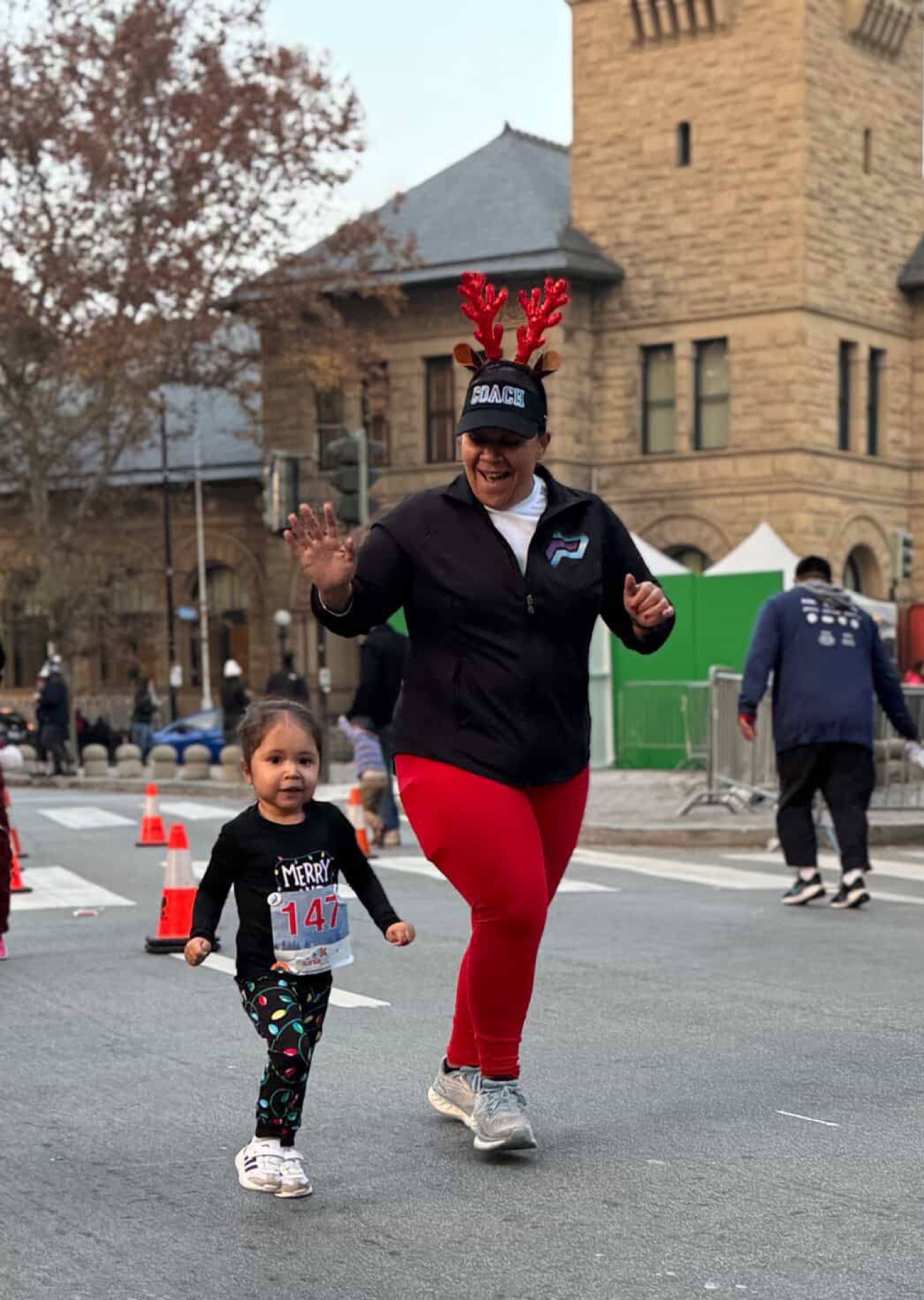 Coach Sabrina in reindeer antlers running alongside a young girl at the Santa Run