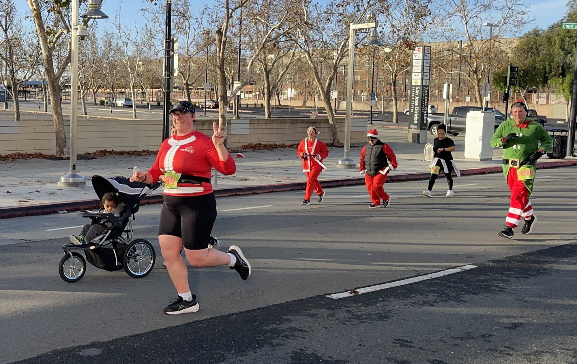 A runner in a Santa shirt pushing a stroller, followed by runners in Santa suits